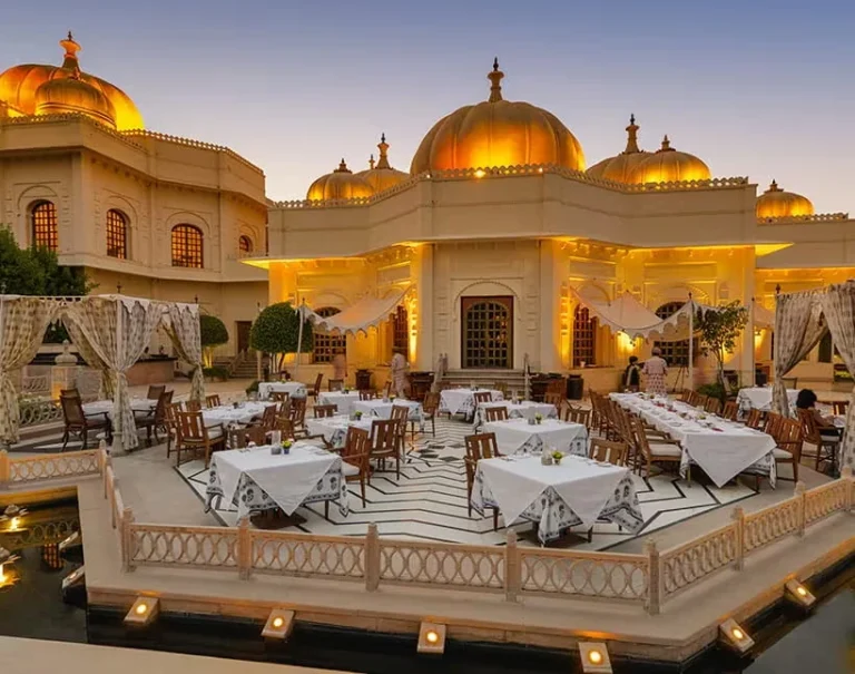 Outdoor dining courtyard at The Oberoi Udaivilas Udaipur, illuminated at dusk with elegant tables and traditional palace domes.