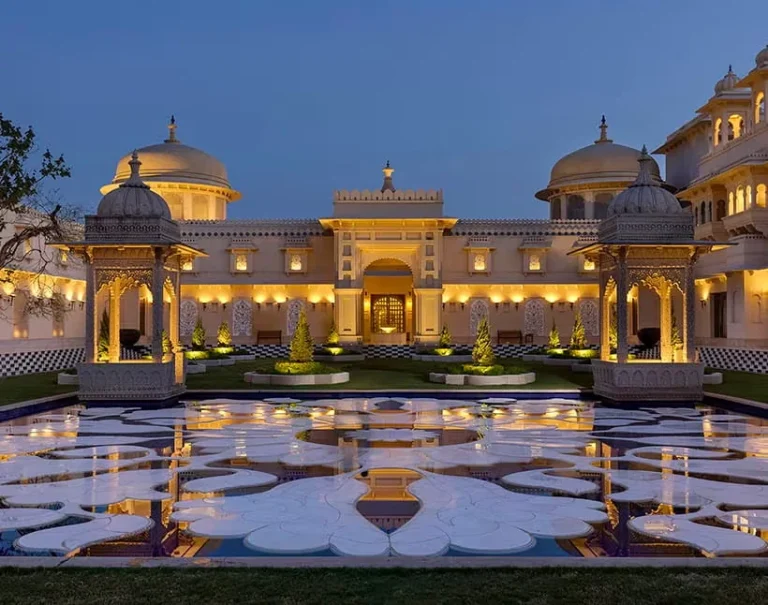 Illuminated palace courtyard at The Oberoi Udaivilas Udaipur, featuring domed pavilions, reflective water and landscaped gardens.