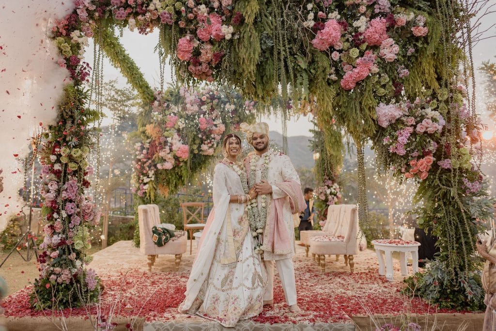 Bride and groom smiling together under a pink and white floral wedding arch at sunset — Desert Pearl Weddings
