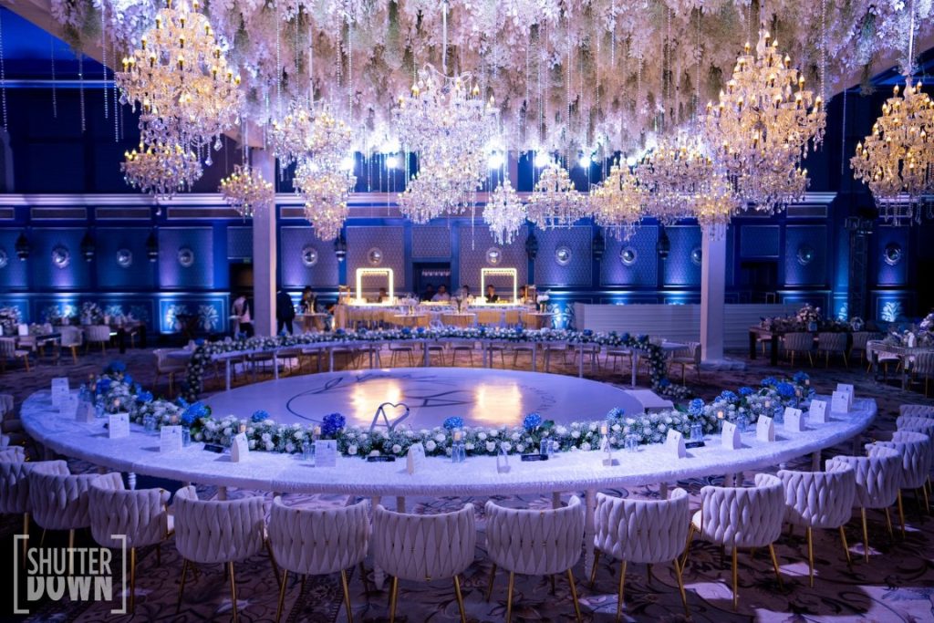 Grand blue reception ballroom with circular head table and crystal chandelier ceiling at Fairmont Jaipur