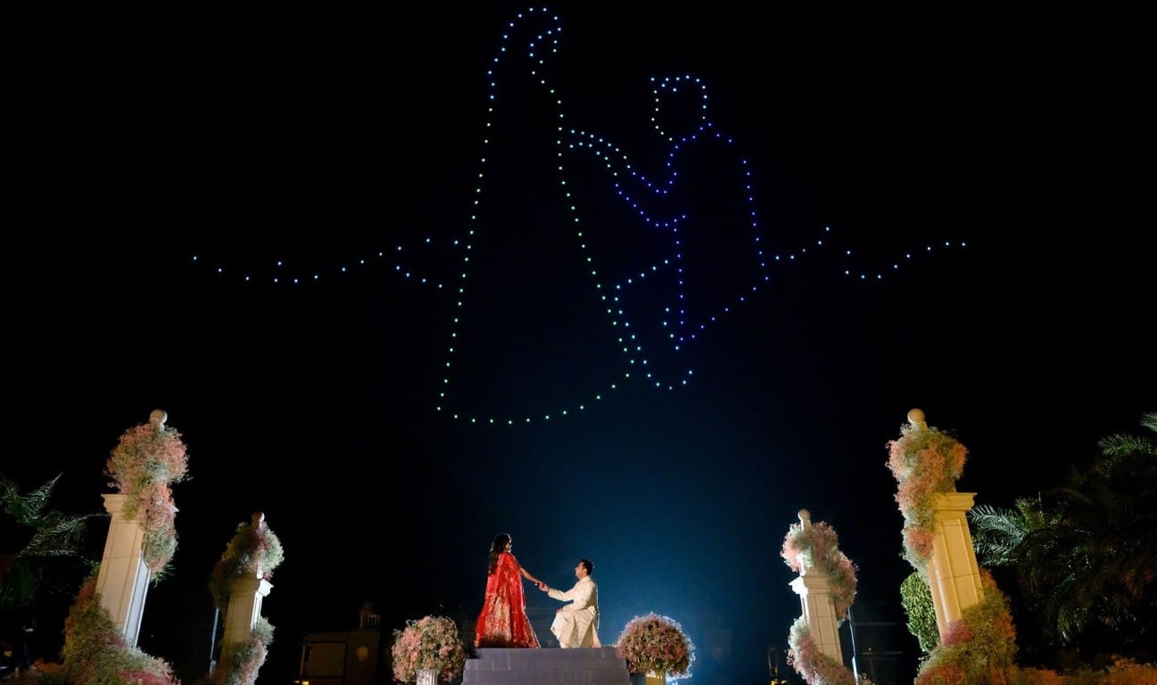 Drone light show forming a couple silhouette above the sky at a luxury destination wedding in Rajasthan, with couple standing on a floral stage — Desert Pearl Weddings Udaipur