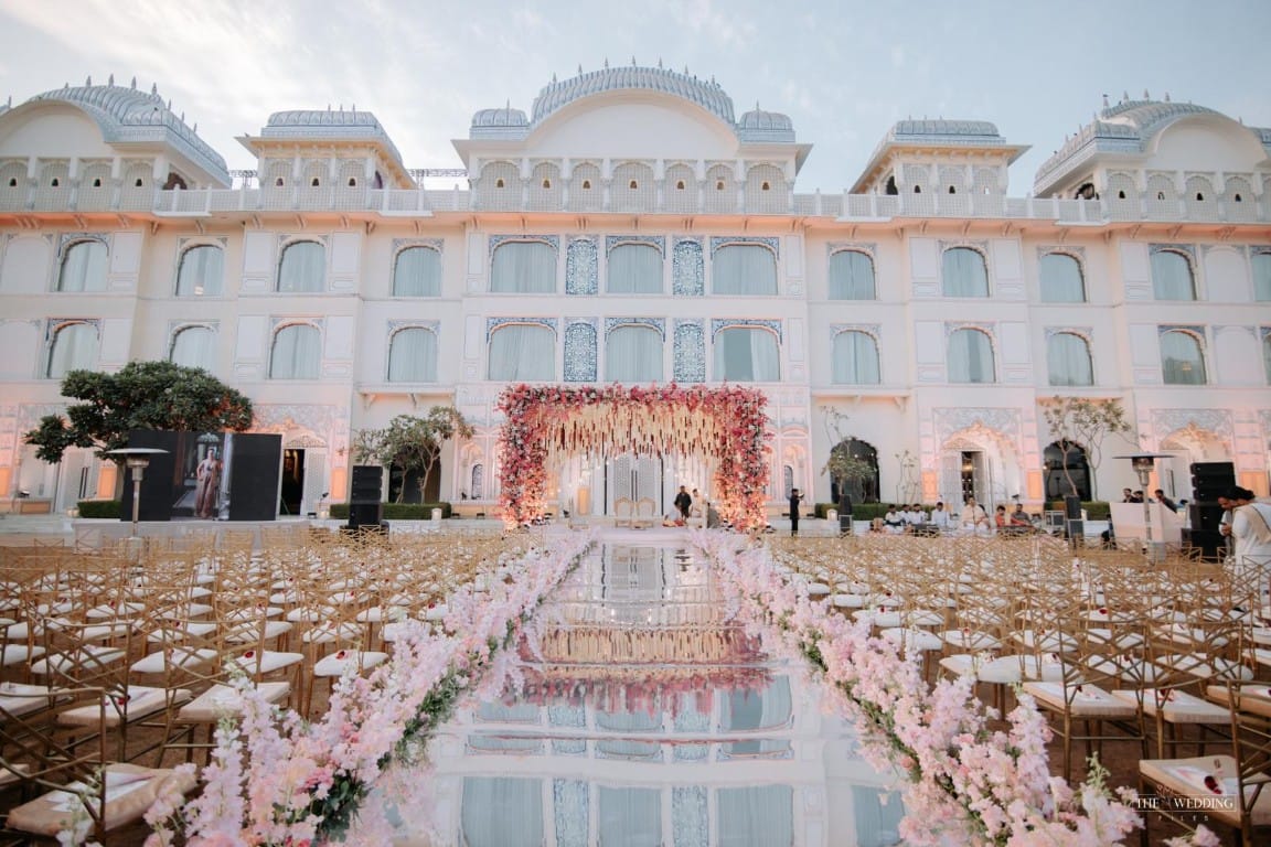Grand outdoor wedding setup with mirror aisle, gold chairs, and floral mandap against a white palace in Rajasthan — Desert Pearl Weddings, destination wedding planner in Udaipur