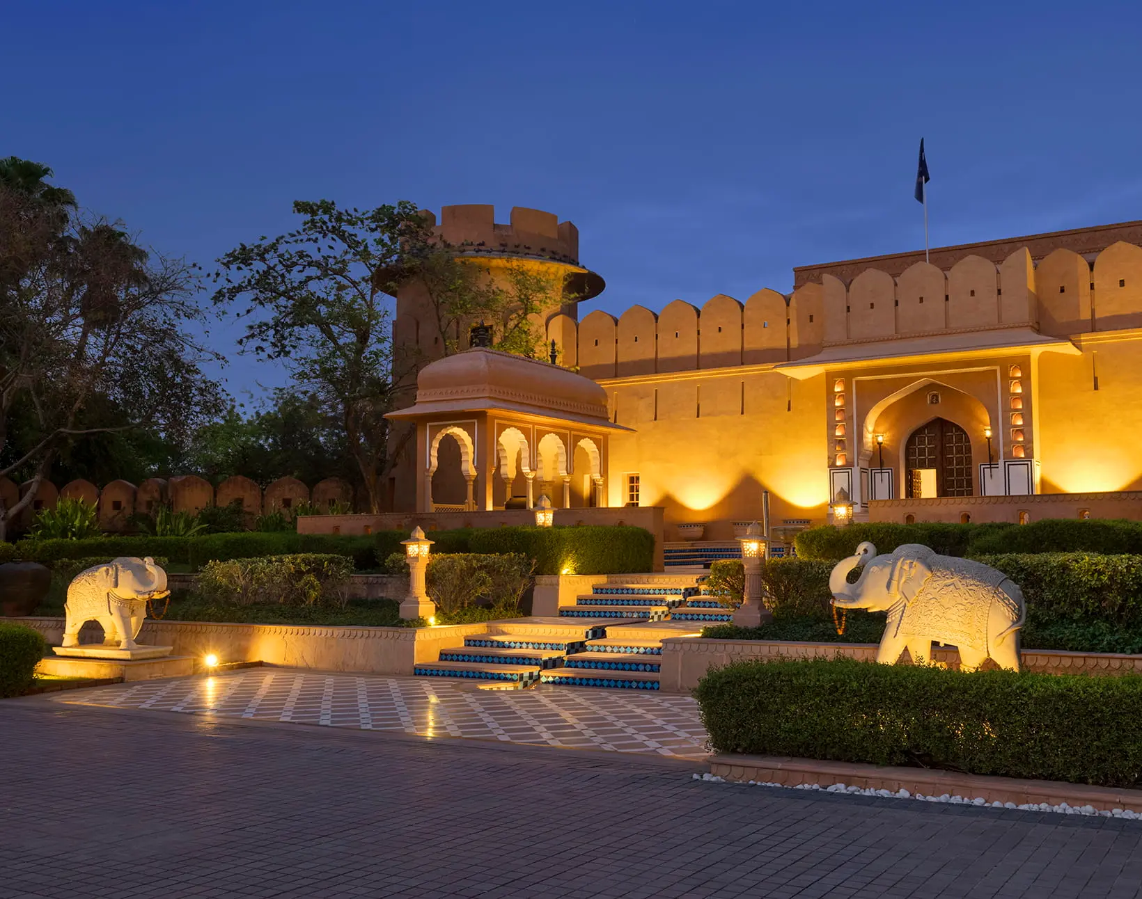 Fort-style entrance with stone elephants illuminated at dusk at The Oberoi Rajvilas, Jaipur