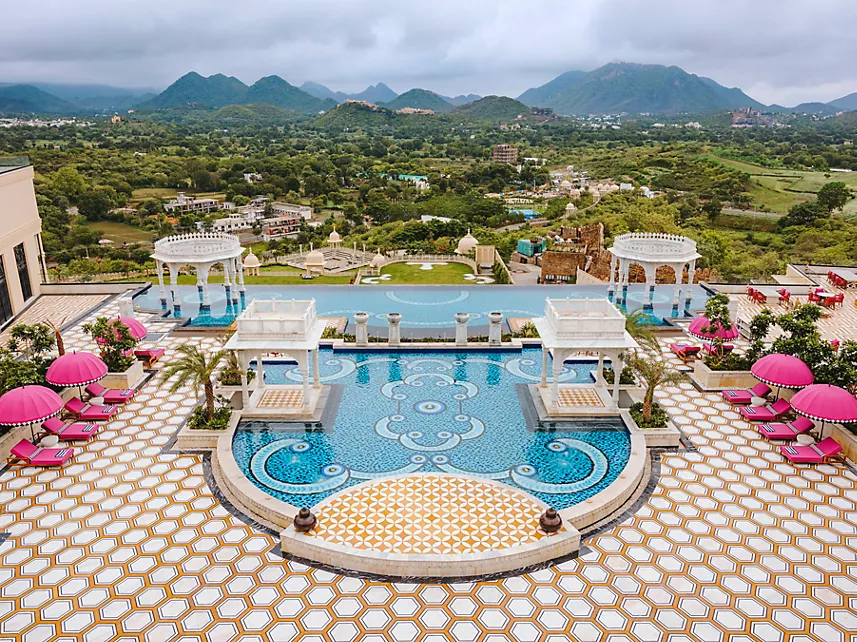 Aerial view of pool with pink umbrellas chattri pavilions and Aravalli mountain backdrop at Fairmont Udaipur Palace