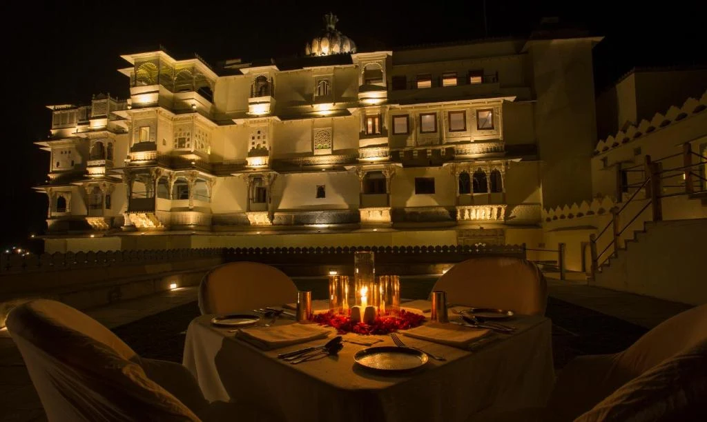 Private candlelit dinner by pool with illuminated heritage palace facade at night at RAAS Devigarh Udaipur