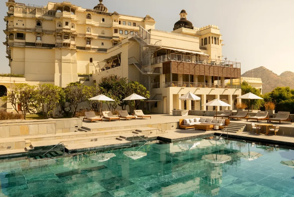 Pool and sun loungers with 18th-century palace facade and Aravalli hills at RAAS Devigarh Udaipur