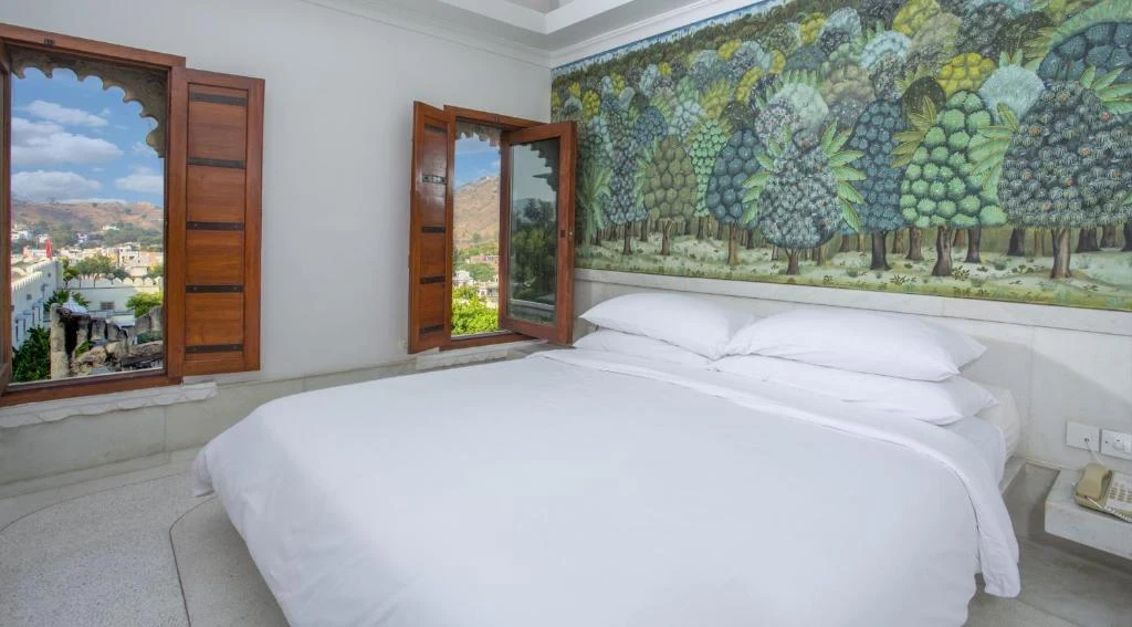 White marble suite with Pichwai-style mural and arched windows overlooking Aravalli hills at RAAS Devigarh Udaipur