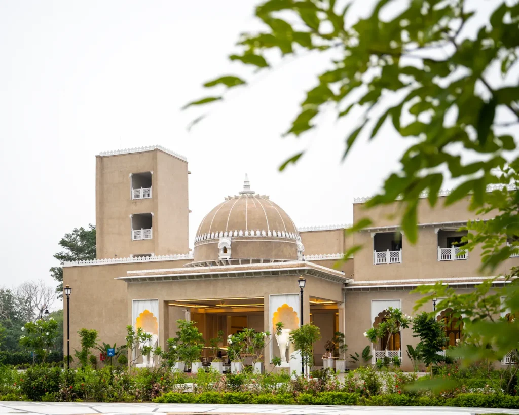 Heritage-style domed entrance pavilion with amber arched interiors and lush garden forecourt at Taj Lalit Bagh Udaipur