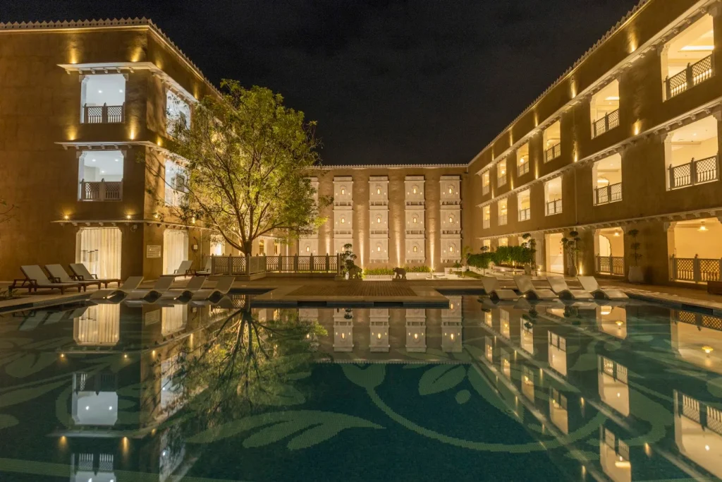 Illuminated palace wings reflected in floral-mosaic pool at night at Taj Lalit Bagh Udaipur