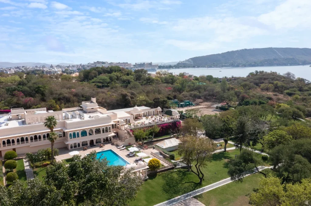 Aerial view of Trident Udaipur pool and gardens with Lake Pichola and City Palace visible in distance