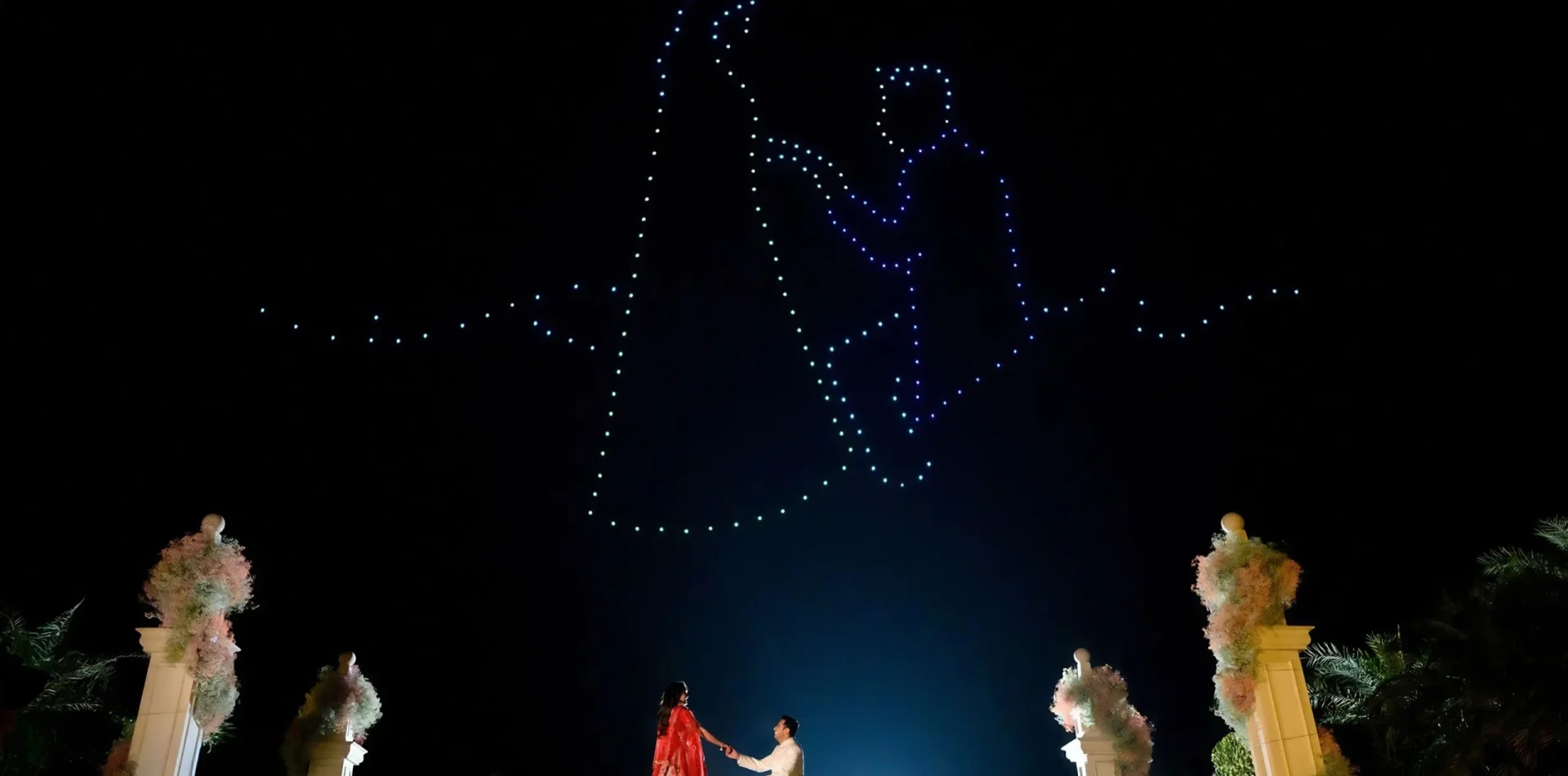 Drone light show above a couple at a night wedding with floral pillars by Desert Pearl Weddings
