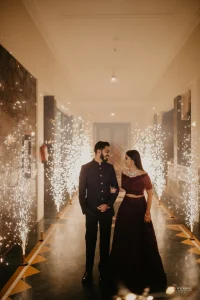 Couple walking through a dramatic indoor sparkler corridor during their wedding reception grand entry, groom in dark navy bandhgala sherwani and bride in maroon lehenga, at a luxury hotel venue in Udaipur Rajasthan