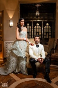 Bride in silver gown and groom in white tuxedo sitting at vintage sofa at Fairmont Jaipur reception