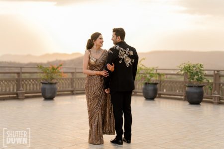 Bride in gold sequin saree and groom in embroidered black suit at rooftop welcome dinner Fairmont Jaipur