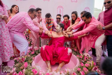 Groom sitting in flower bathtub surrounded by family during Haldi ceremony at Fairmont Jaipur wedding