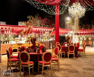 Red and gold outdoor Sangeet dinner setup with chandeliers at Fairmont Jaipur wedding