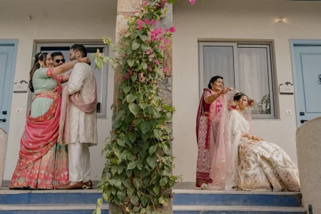 Creative split frame wedding photograph showing a couple sharing a warm hug outside a venue with blooming pink bougainvillea on the left, and a mother carefully draping her daughter's dupatta as the bride sits in her white floral embroidered bridal lehenga on the right, at a destination wedding in Rajasthan