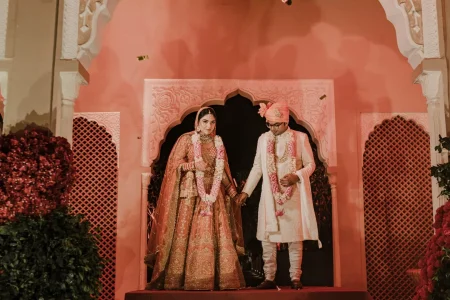 Bride in orange lehenga and groom in white sherwani exiting Rajasthani palace wedding mandap after ceremony at luxury destination wedding in Rajasthan