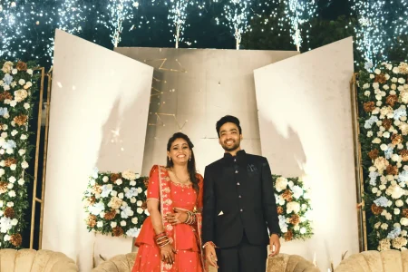 Bride in red lehenga and groom in black bandhgala suit on stage with cold pyro sparklers and blue white floral arrangements at engagement night destination wedding in Rajasthan