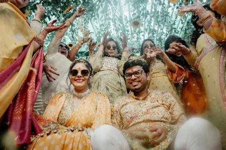 Bride and groom celebrating haldi with friends showering flower petals under sunflower arch at destination wedding in Rajasthan