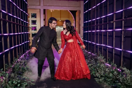 Bride in red sequin lehenga and groom in black sherwani making grand entrance through LED lit tunnel at Nikita Vedant sangeet night, destination wedding in Rajasthan planned by Desert Pearl Weddings