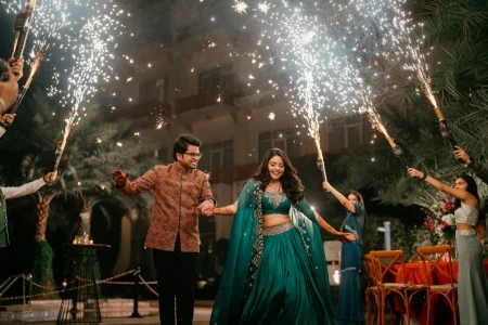 Bride in teal cape lehenga and groom in printed sherwani smiling during sparkler tunnel entrance at Nikita Vedant cocktail night, luxury destination wedding in Rajasthan by Desert Pearl Weddings