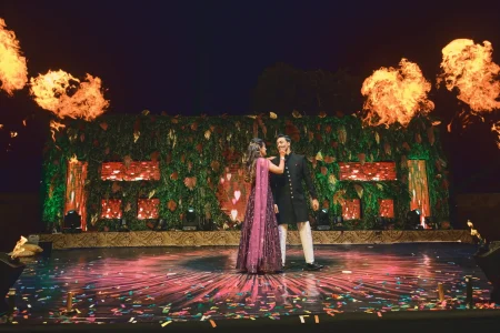 Couple dancing on sangeet night stage with dramatic fire cannon effects and green tropical leaf backdrop with heart projections at luxury destination wedding in Rajasthan by Desert Pearl Weddings